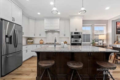 Kitchen featuring appliances with stainless steel finishes, white cabinetry, light stone countertops, tasteful backsplash, and a breakfast bar