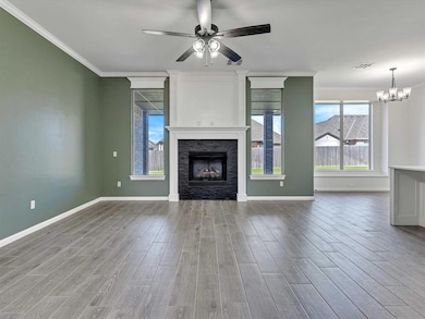 Unfurnished living room featuring crown molding, a fireplace, wood finished floors, a ceiling fan, and a chandelier