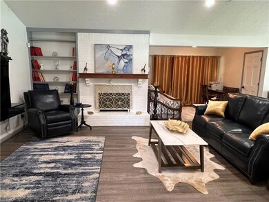 Living room with a brick fireplace, wood finished floors, and a textured ceiling