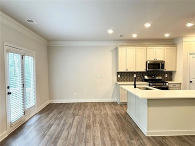 Kitchen featuring stainless steel appliances, light countertops, backsplash, wood finished floors, and crown molding