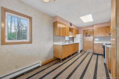 Kitchen with baseboard heating, light countertops, white appliances, wallpapered walls, and plenty of natural light
