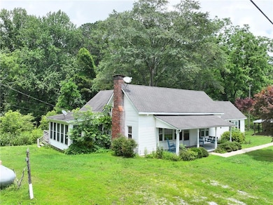 View of front of property with a porch, a front yard, a chimney, roof with shingles, and a sunroom