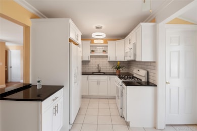 Kitchen with ornamental molding, decorative backsplash, white appliances, light tile patterned floors, and white cabinets
