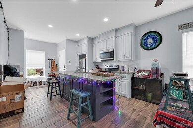 Kitchen with light wood-type flooring, white cabinetry, open shelves, appliances with stainless steel finishes, and a kitchen breakfast bar
