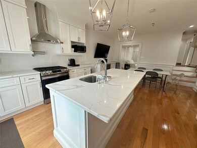 Kitchen with light wood-style flooring, ornamental molding, wall chimney exhaust hood, appliances with stainless steel finishes, and a sink