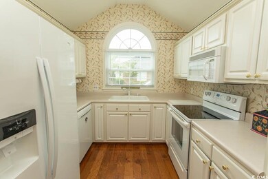 Kitchen with white appliances, wallpapered walls, a sink, vaulted ceiling, and dark wood finished floors
