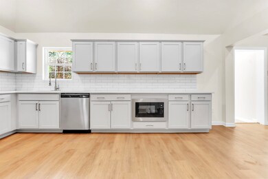 Kitchen featuring dishwasher, black microwave, light wood finished floors, a sink, and tasteful backsplash