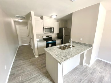 Kitchen with stainless steel appliances, wood tiled floors, light stone counters, a peninsula, and white cabinets