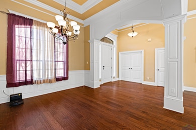 Empty room featuring arched walkways, a decorative wall, dark wood finished floors, crown molding, and a chandelier