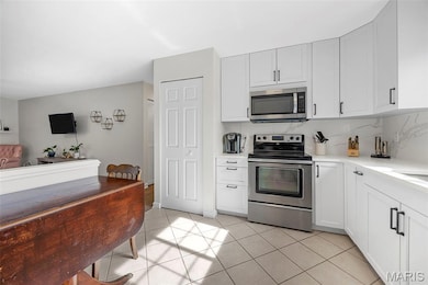 Kitchen with appliances with stainless steel finishes, backsplash, white cabinets, and light tile patterned flooring