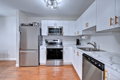 Kitchen with appliances with stainless steel finishes, white cabinets, light wood-type flooring, and light stone countertops