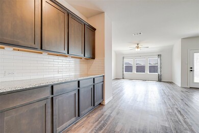 Kitchen featuring light wood-type flooring, light stone counters, ceiling fan, and dark brown cabinetry
