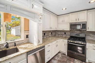 Kitchen with appliances with stainless steel finishes, tasteful backsplash, recessed lighting, light stone countertops, and cream cabinets