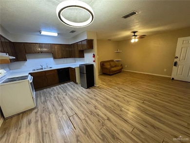 Kitchen with white electric range oven, ventilation hood, freestanding refrigerator, a sink, and light wood-style floors