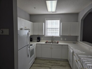 Kitchen featuring white appliances, light countertops, white cabinetry, light wood finished floors, and a textured ceiling