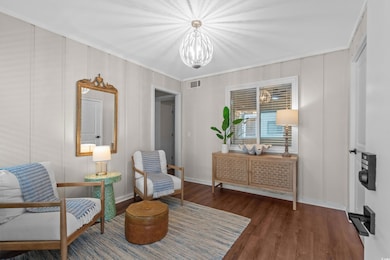 Living area featuring a chandelier, wood finished floors, baseboards, and ornamental molding