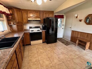 Kitchen with freestanding refrigerator, white range with electric cooktop, under cabinet range hood, a sink, and brown cabinets