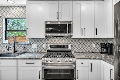 Kitchen with appliances with stainless steel finishes, white cabinets, dark stone countertops, and decorative backsplash