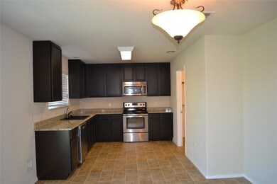 Kitchen with stainless steel appliances, light stone counters, light tile flooring, and sink