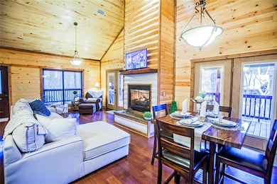 Living room featuring wood walls, dark wood-type flooring, high vaulted ceiling, a stone fireplace, and wood ceiling