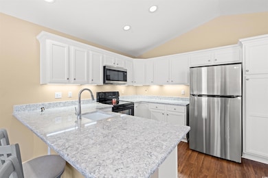 Kitchen featuring white cabinetry, stainless steel appliances, lofted ceiling, a peninsula, and a kitchen bar