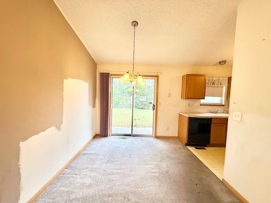 Kitchen featuring a textured ceiling, a chandelier, light colored carpet, brown cabinetry, and light countertops