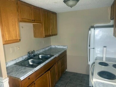 Kitchen with brown cabinetry, a textured ceiling, light countertops, white electric range, and dark tile patterned floors