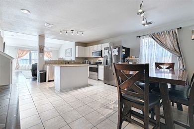 Kitchen with stainless steel appliances, white cabinetry, a textured ceiling, light tile patterned floors, and healthy amount of natural light