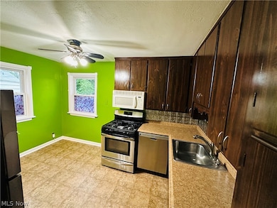 Kitchen with a textured ceiling, backsplash, dark brown cabinets, light tile floors, appliances with stainless steel finishes, and ceiling fan