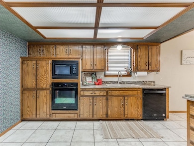 Kitchen featuring wallpapered walls, black appliances, brown cabinetry, light countertops, and light tile patterned floors