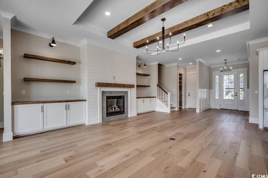 Unfurnished living room with a chandelier, light wood-style floors, beam ceiling, crown molding, and a glass covered fireplace