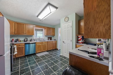 Kitchen featuring appliances with stainless steel finishes, a sink, light countertops, brown cabinetry, and a textured ceiling