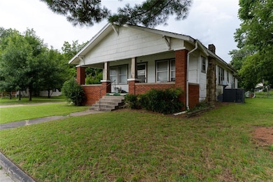 View of front of home with brick siding, a chimney, a porch, and a front lawn