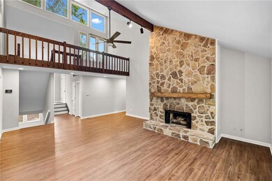 Unfurnished living room with wood finished floors, a ceiling fan, high vaulted ceiling, a stone fireplace, and stairs