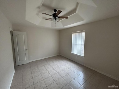 Unfurnished room featuring a tray ceiling, light tile patterned floors, ceiling fan, and baseboards