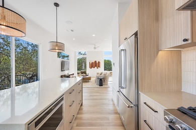 Kitchen featuring light brown cabinets, pendant lighting, light stone counters, open floor plan, and stainless steel appliances
