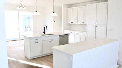 Kitchen with white cabinetry, decorative light fixtures, light wood finished floors, a center island with sink, and dishwasher
