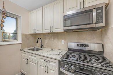 Kitchen featuring stainless steel appliances, tasteful backsplash, light stone countertops, and white cabinets