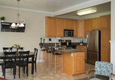 Kitchen with appliances with stainless steel finishes, a peninsula, a breakfast bar, ornamental molding, and brown cabinets