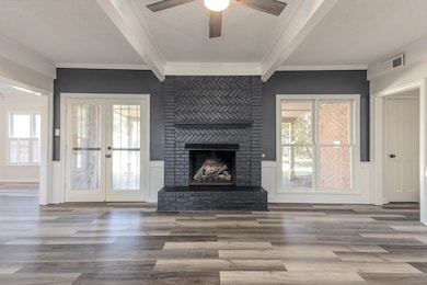 Unfurnished living room with beamed ceiling, a textured ceiling, a fireplace, wood finished floors, and ceiling fan