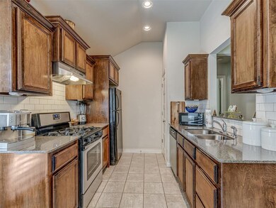 Kitchen with black appliances, under cabinet range hood, tasteful backsplash, stone countertops, and vaulted ceiling