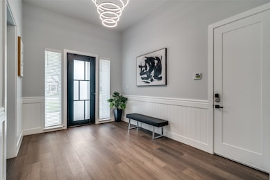 Entrance foyer with a chandelier, wood finished floors, and wainscoting