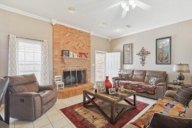 Living room with a fireplace, light tile patterned flooring, brick wall, ceiling fan, and ornamental molding