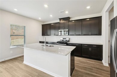 Kitchen with stainless steel appliances, decorative backsplash, light stone countertops, a center island with sink, and light wood finished floors