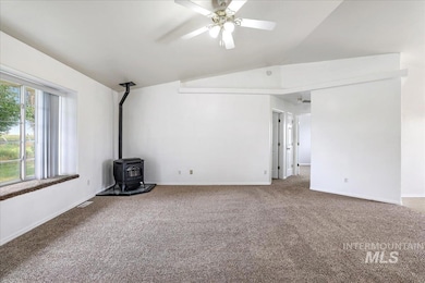 Unfurnished living room featuring lofted ceiling, a wood stove, carpet flooring, and ceiling fan