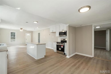 Kitchen featuring baseboards, stainless steel appliances, white cabinetry, light wood-style floors, and backsplash