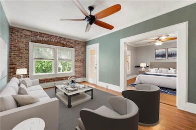 Living area featuring brick wall, light wood-style floors, a ceiling fan, ornamental molding, and baseboards