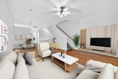 This modern living room features an open floor plan with hardwood floors and neutral walls. It includes a cozy seating area, a ceiling fan, and a large TV setup. Adjacent is a stylish dining area, and the space is accented with contemporary decor and ample natural light. A staircase leads to the upper level.