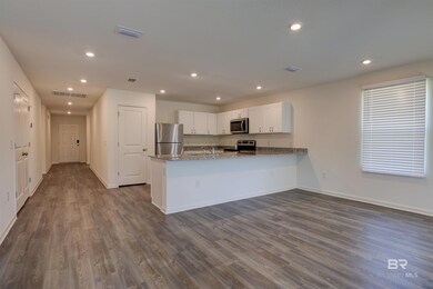 Kitchen featuring stainless steel appliances, kitchen peninsula, light stone countertops, white cabinetry, and dark hardwood / wood-style flooring