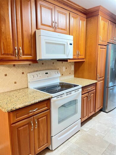 Kitchen with white range with electric stovetop, refrigerator, brown cabinetry, and decorative backsplash